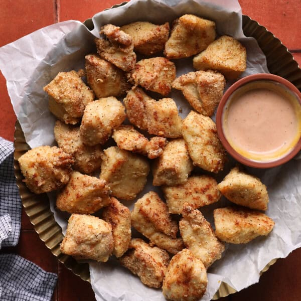 Air fryer chicken bites served in a basket with dipping sauce.