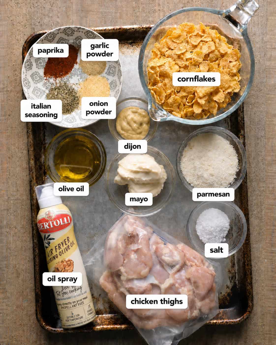 Ingredients for baked cornflake chicken thighs, including cornflakes, Parmesan, chicken thighs, mayo, Dijon mustard, olive oil, and seasonings