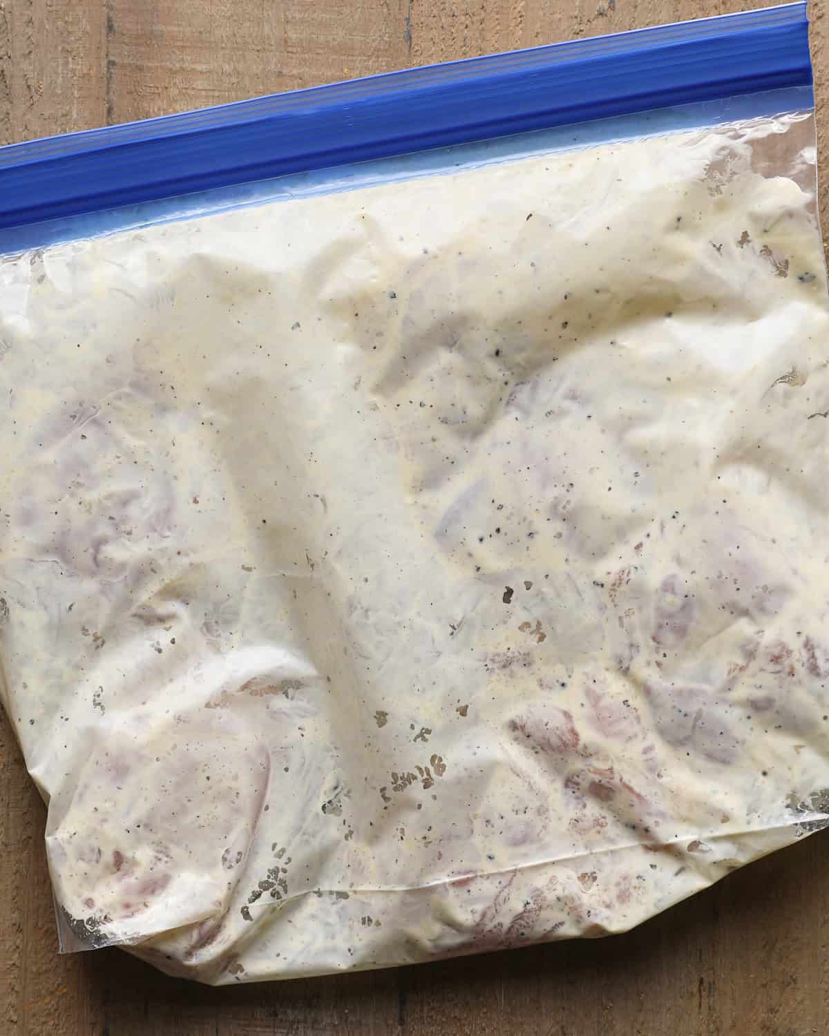 Boneless chicken thighs coated with the mayonnaise-Dijon binder in a zip-top bag.