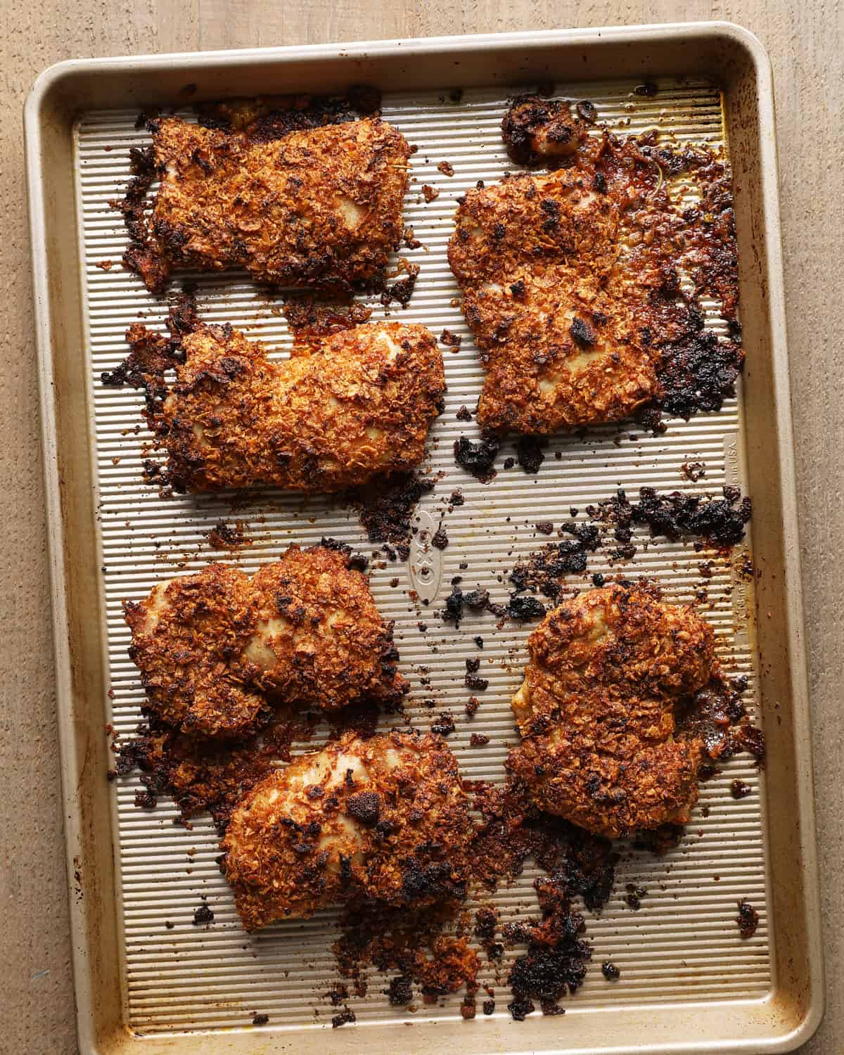 Baked cornflake chicken thighs with a browned coating on the baking sheet.