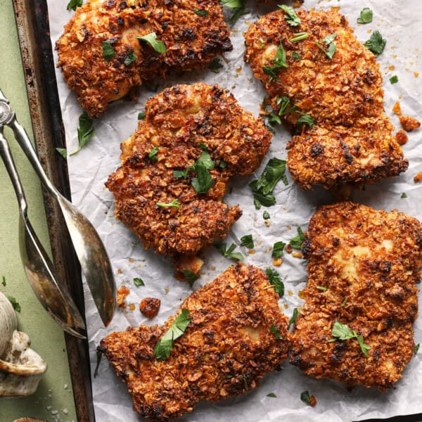 Crispy baked cornflake chicken thighs with chopped parsley on a parchment-lined sheet pan.