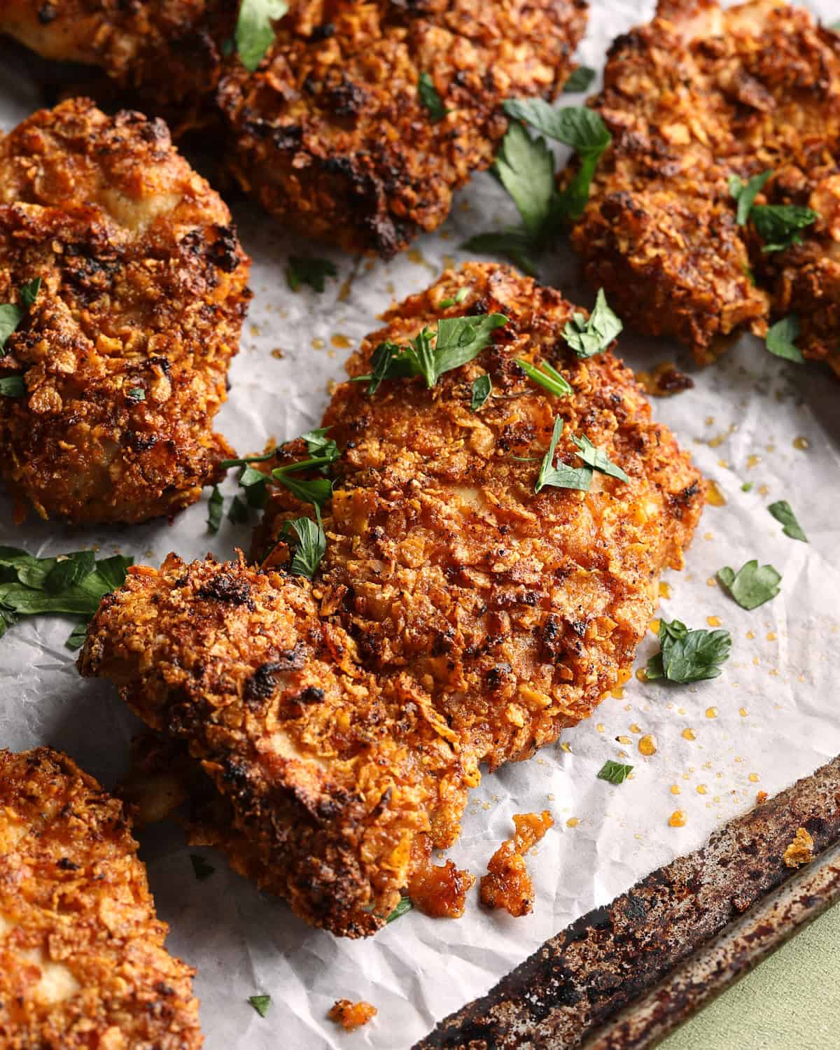 Close-up of crispy baked cornflake chicken thighs with a browned Parmesan-cornflake coating and chopped parsley.