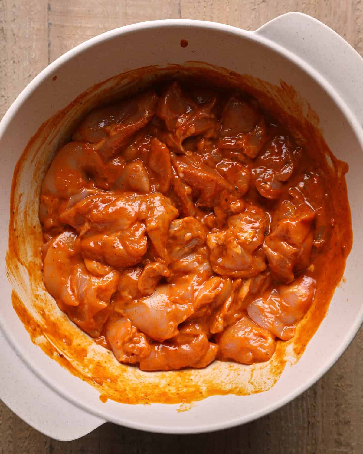Chicken thigh pieces tossed with chipotle lime marinade in a large mixing bowl.