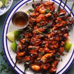 Cropped overhead photo of grilled chipotle lime chicken skewers served with lime wedges and extra hot honey sauce.
