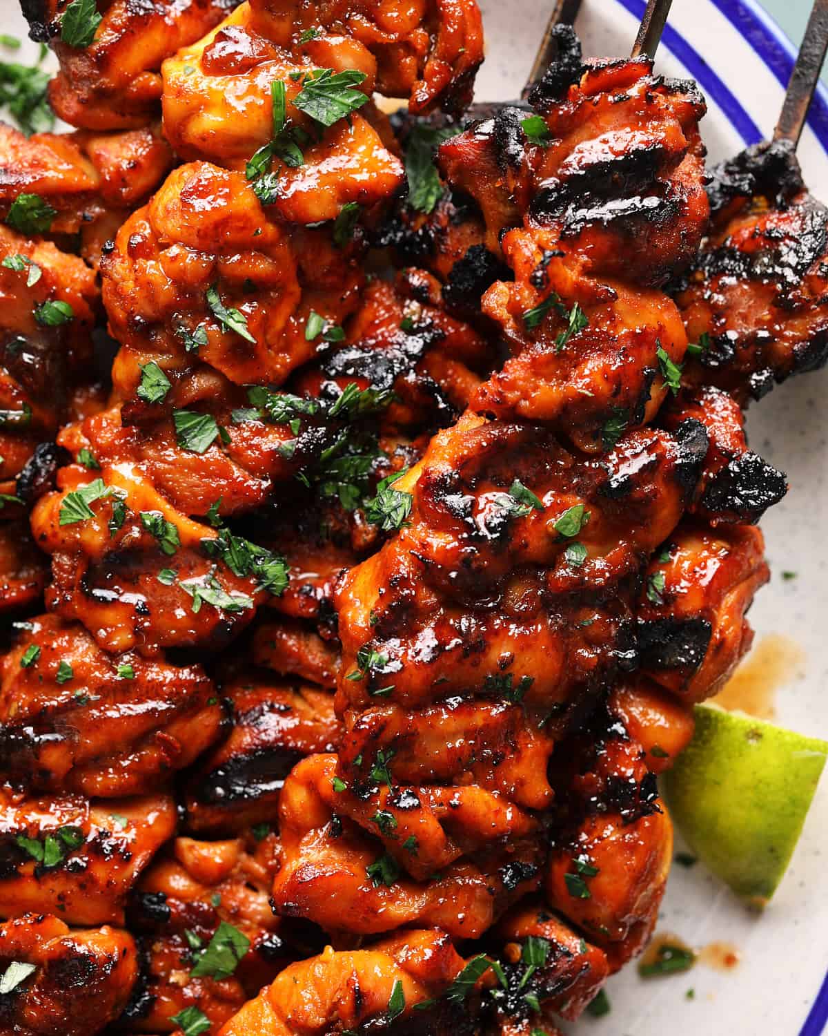 Close-up of grilled chipotle lime chicken skewers with charred edges, hot honey glaze, fresh parsley, and lime wedges.
