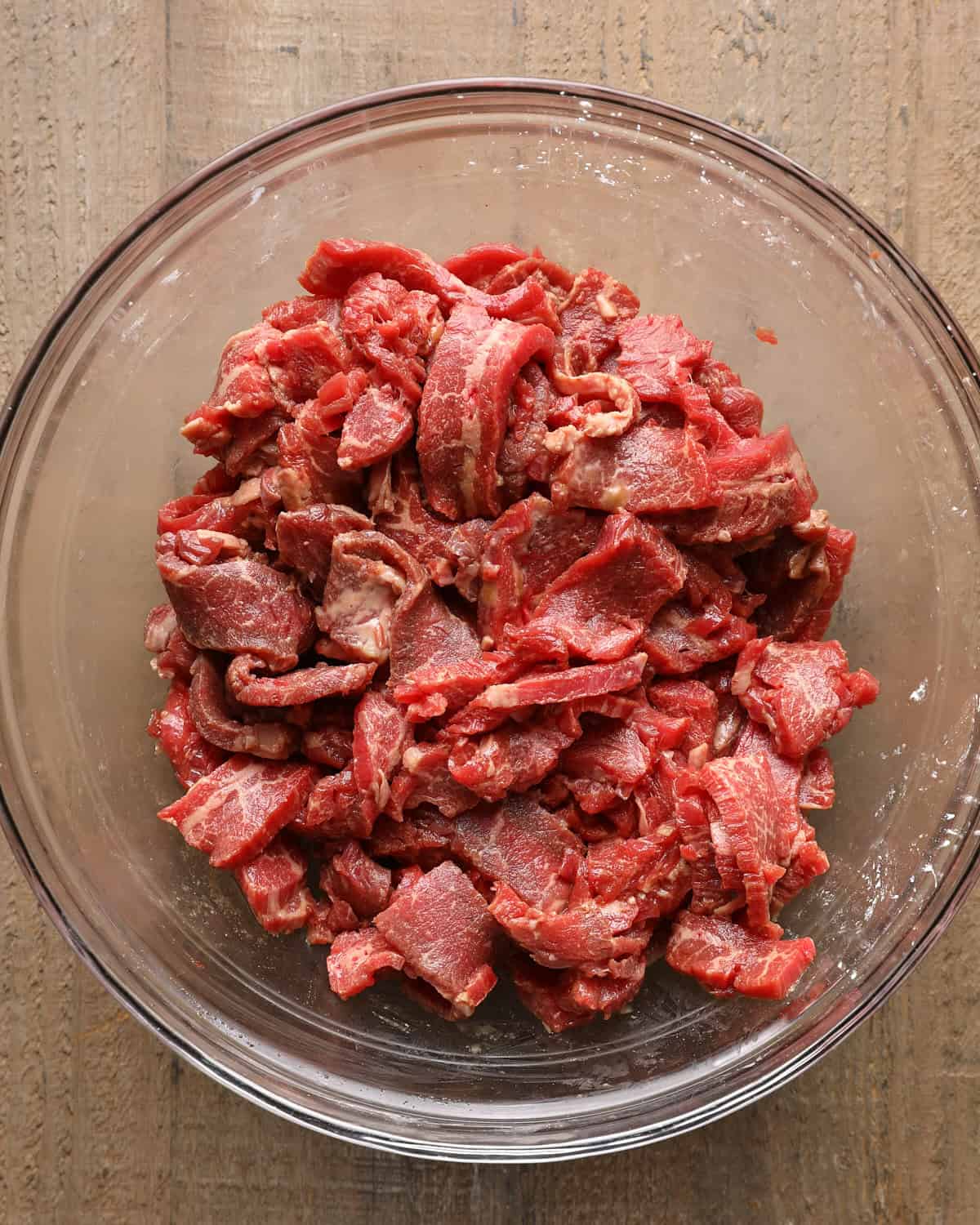 Thinly sliced steak tossed with sauce and cornstarch in a glass bowl.