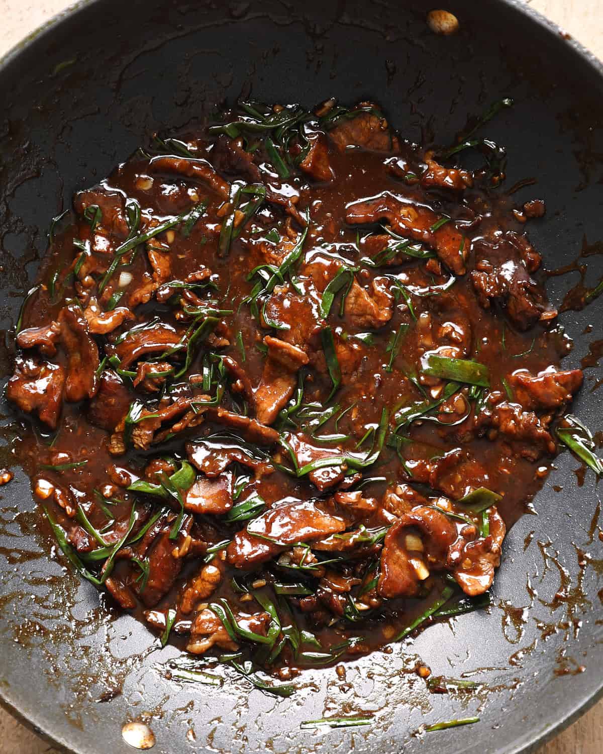 Mongolian beef simmering in a glossy sauce with green onions in a skillet.