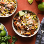 Cropped overhead photo of a street corn chicken rice bowl with grilled chicken, corn salsa, crema, Cotija cheese, and lime wedges.