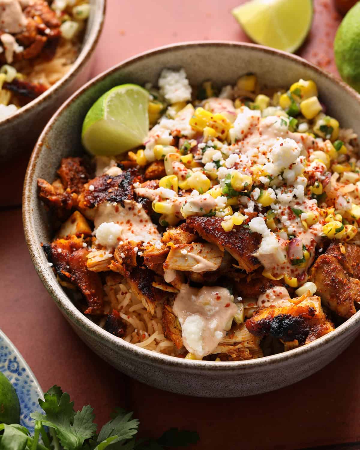 Close-up of a street corn chicken rice bowl topped with grilled chicken, corn salsa, crema, Cotija cheese, and Tajín.