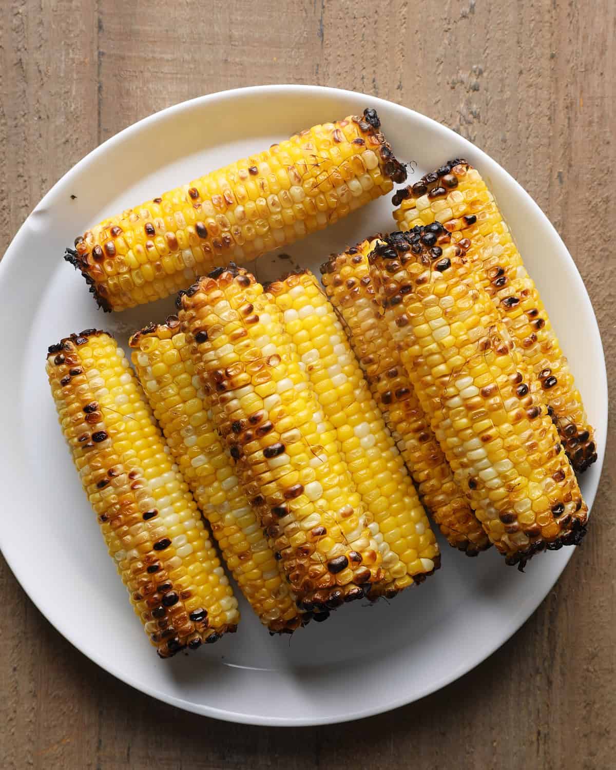 Charred broiled corn on the cob arranged on a white plate.