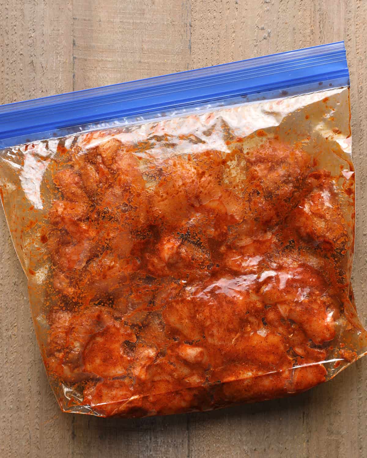Chicken thighs coated in seasoning, oil, and adobo sauce inside a zip-top bag.