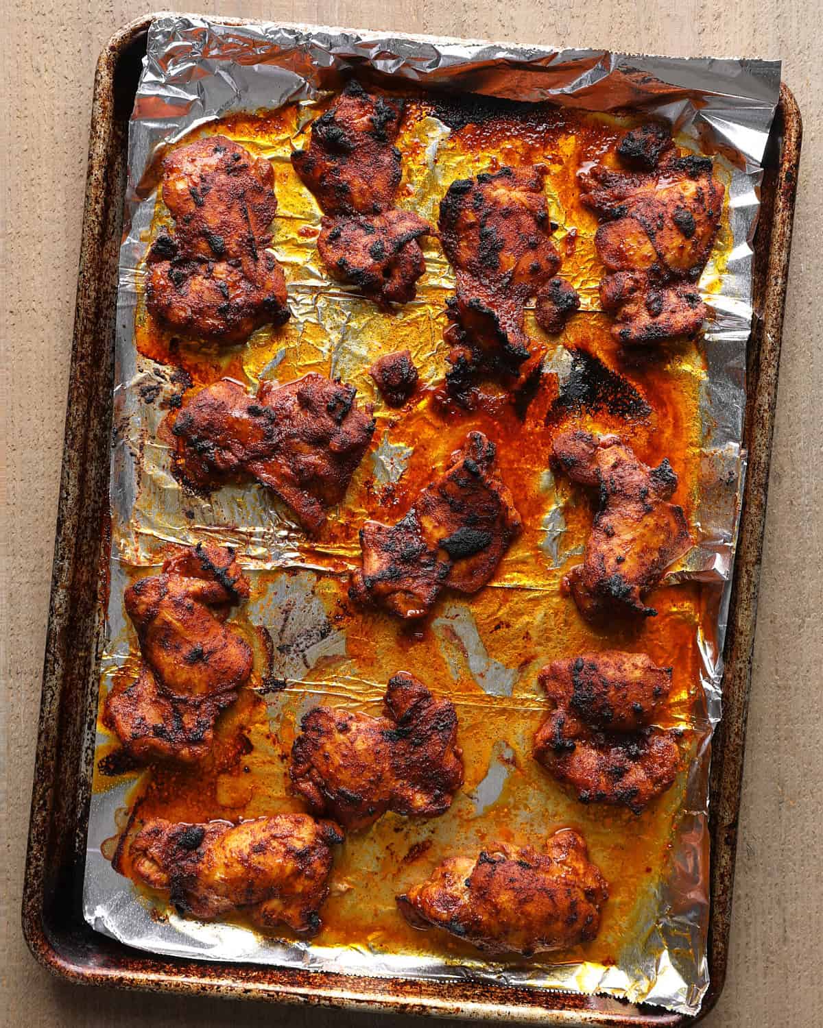 Broiled chicken thighs on a foil-lined sheet pan, charred on top.