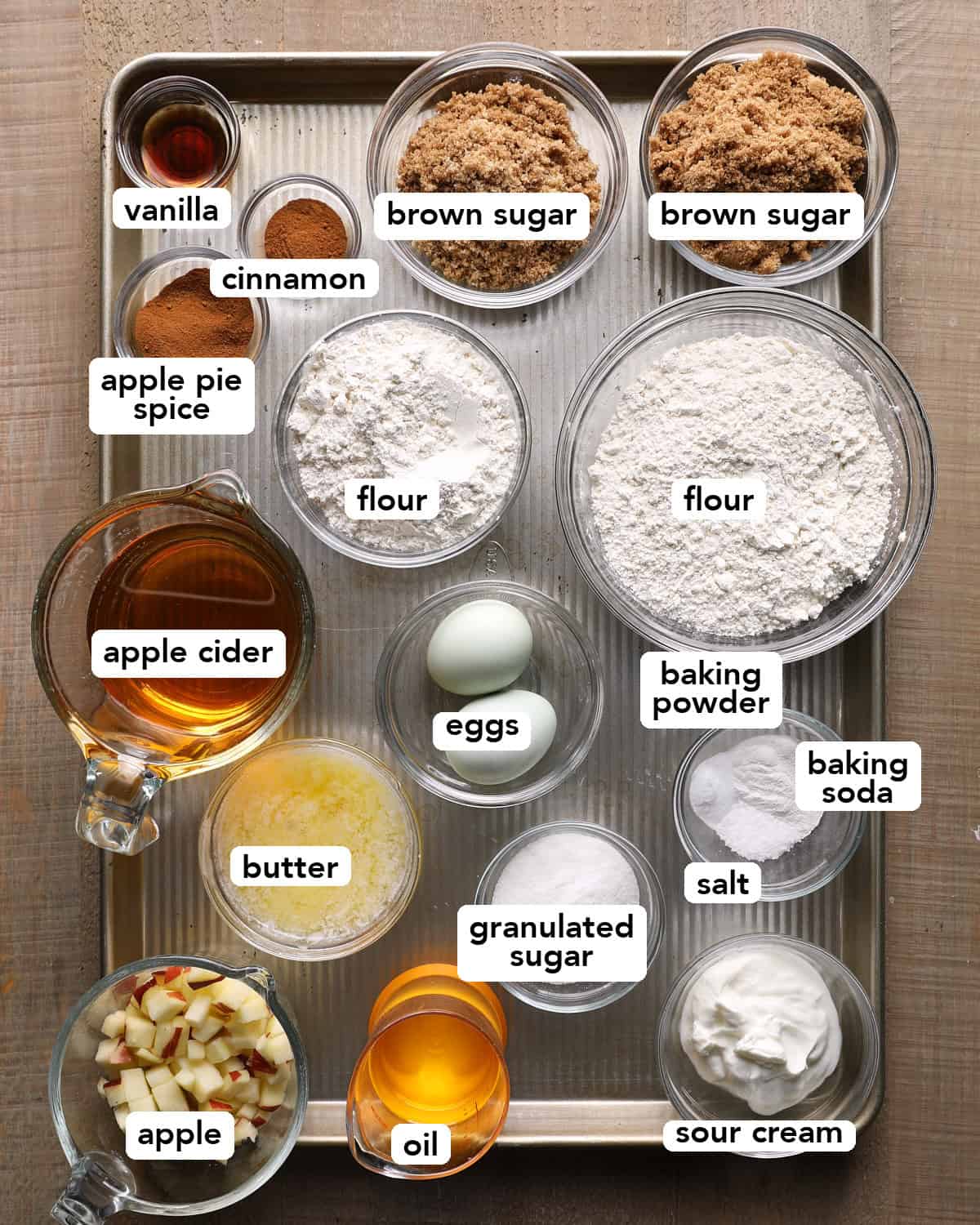 Apple cider, diced apple, flour, sugars, oil, butter, sour cream, eggs, vanilla, spices, leaveners, and salt for apple cider muffins.