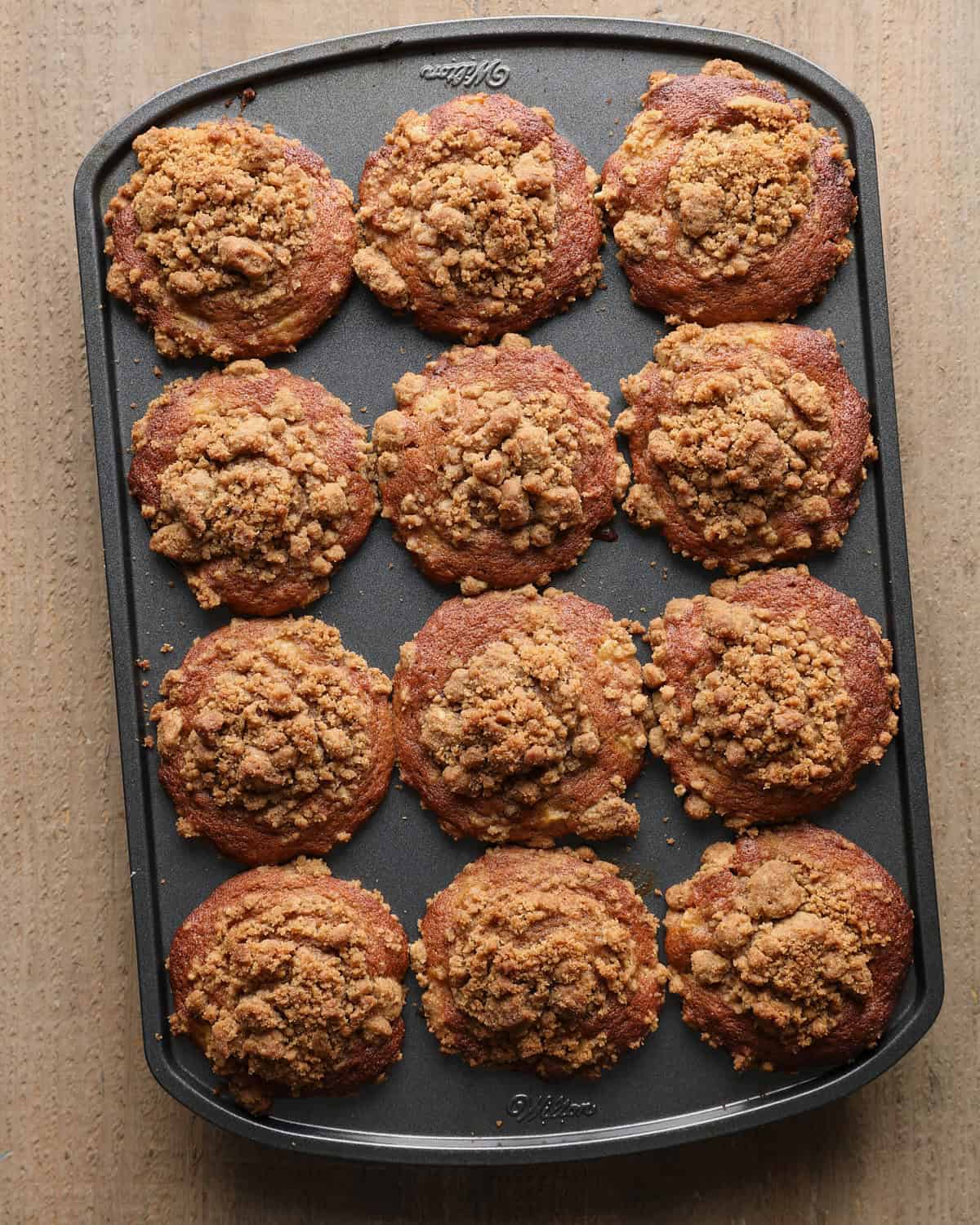 Twelve baked apple cider muffins with tall browned tops and cinnamon crumb in the muffin pan.