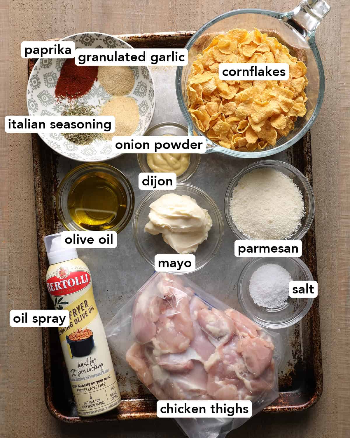 Ingredients for baked cornflake chicken thighs, including cornflakes, Parmesan, chicken thighs, mayo, Dijon mustard, olive oil, and seasonings
