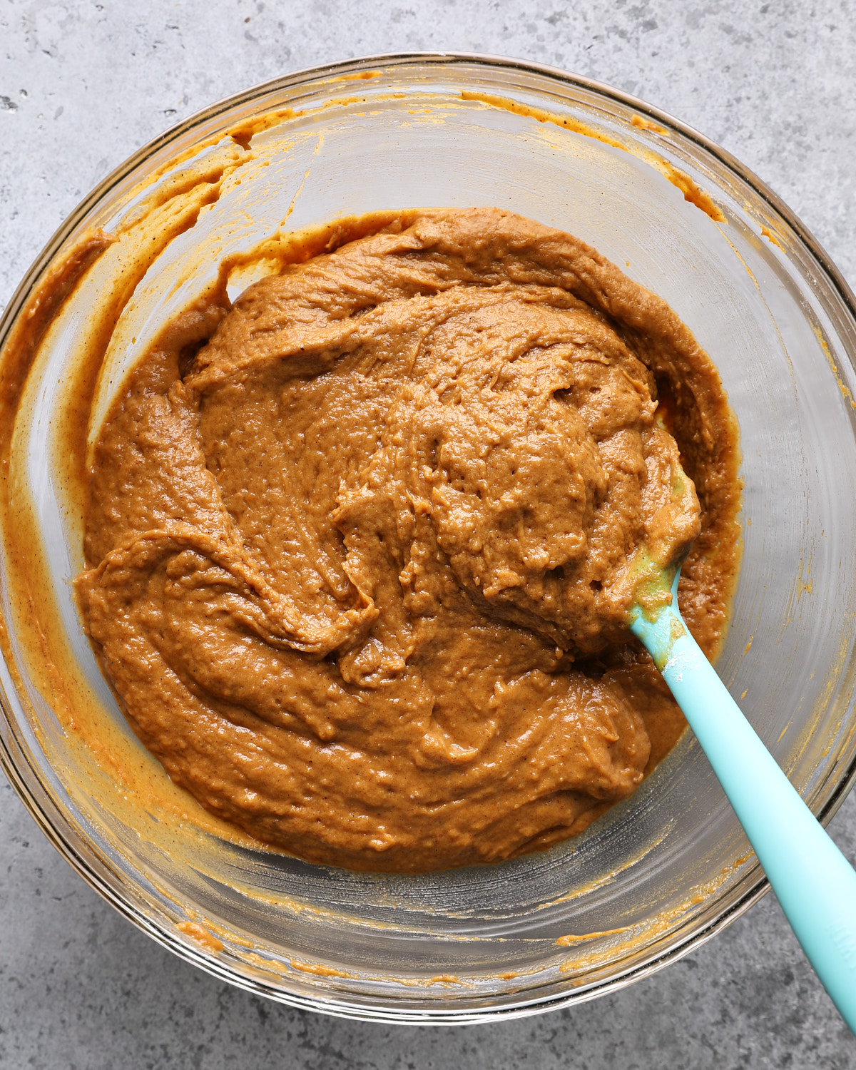 Thick pumpkin coffee cake batter in a glass mixing bowl with a spatula.