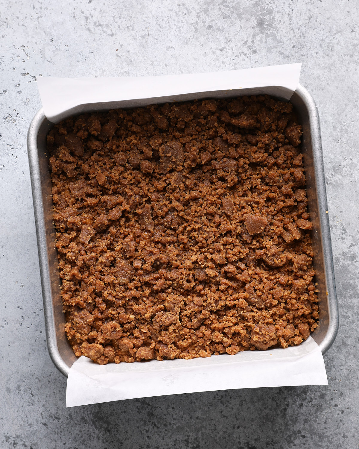 Unbaked pumpkin coffee cake in a parchment-lined square pan covered with crumb topping.
