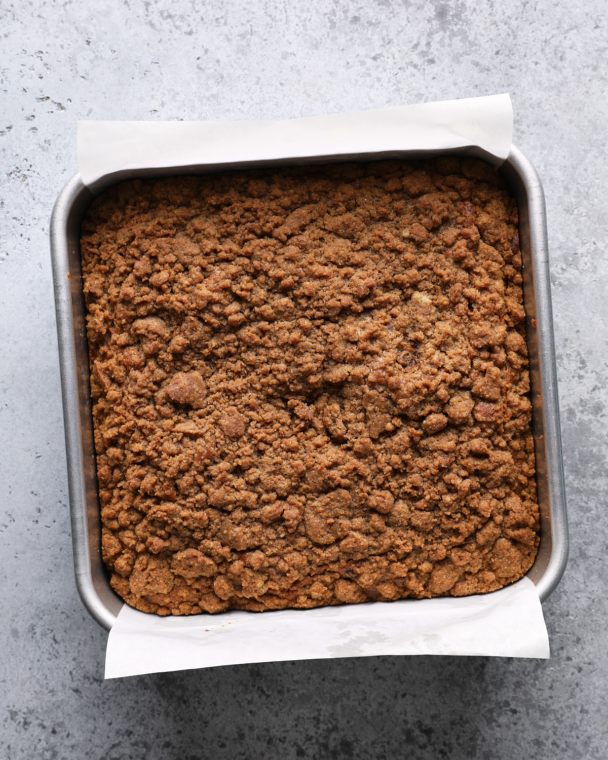 Baked pumpkin coffee cake with golden-brown crumbs in a parchment-lined square pan.