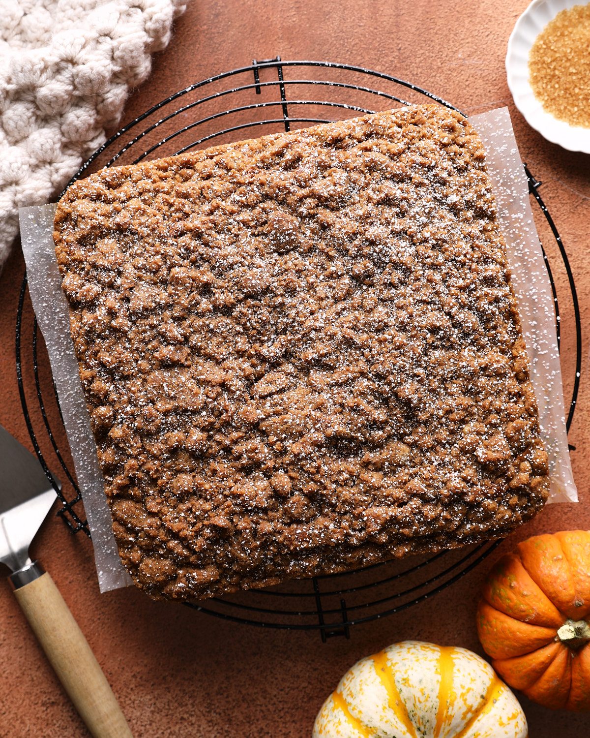 Whole pumpkin coffee cake with a thick brown sugar crumb topping on a cooling rack.