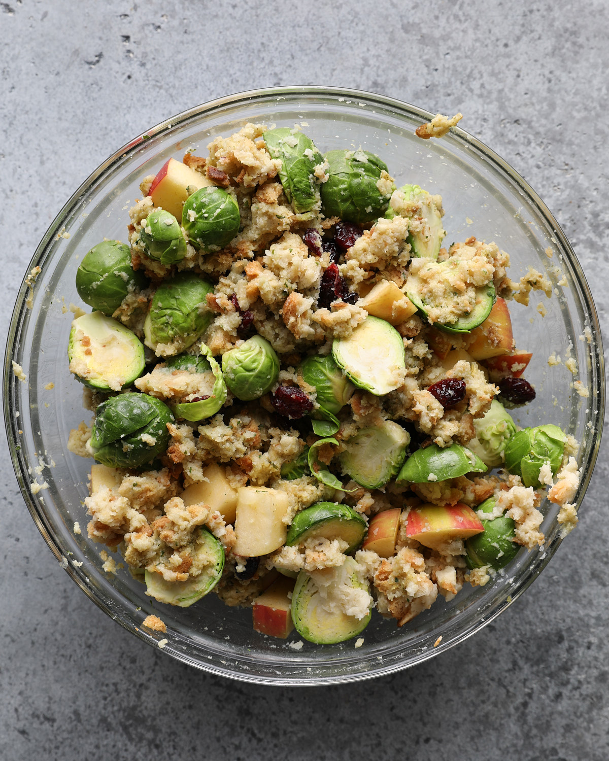 Stuffing mixed with halved Brussels sprouts, diced apple, dried cranberries, and Parmesan in a glass bowl.