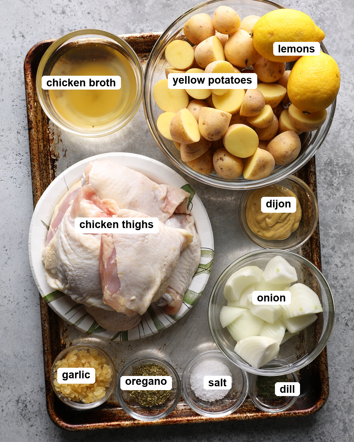 Labeled ingredients for slow cooker Greek lemon chicken and potatoes arranged on a table.
