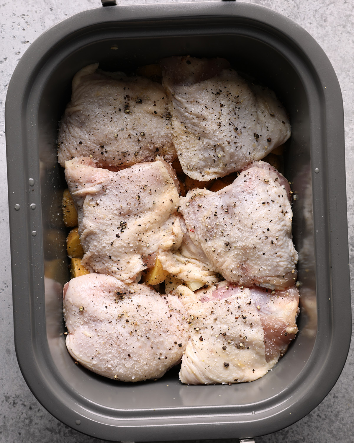 Raw bone-in chicken thighs arranged skin-side up over potatoes in a slow cooker.