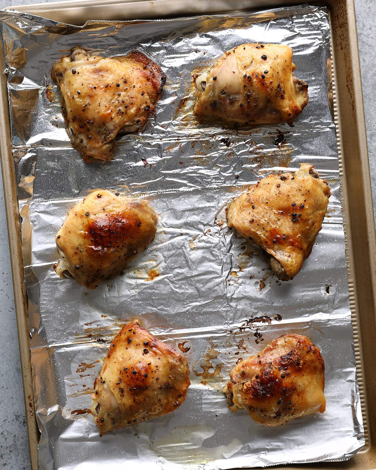 Greek lemon chicken thighs browned beneath the broiler on a foil-lined pan.