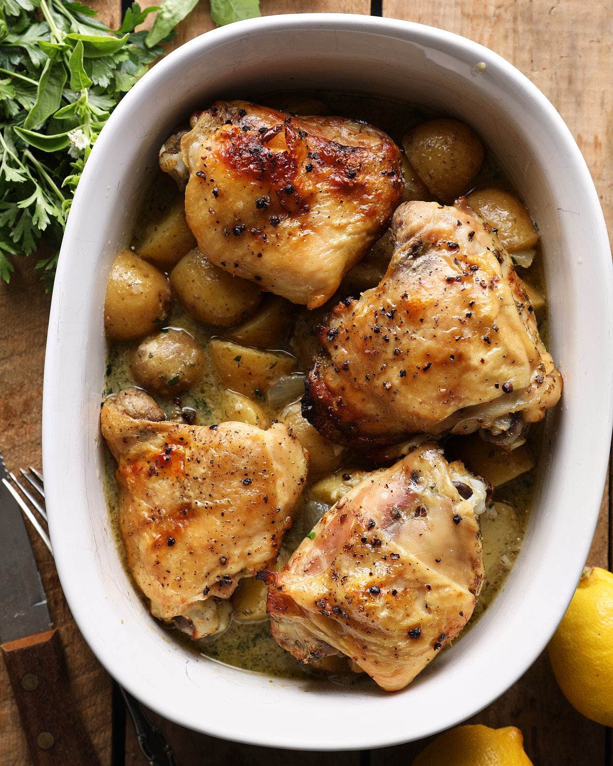 Broiled bone-in chicken thighs with potatoes and lemon broth in a white dish.