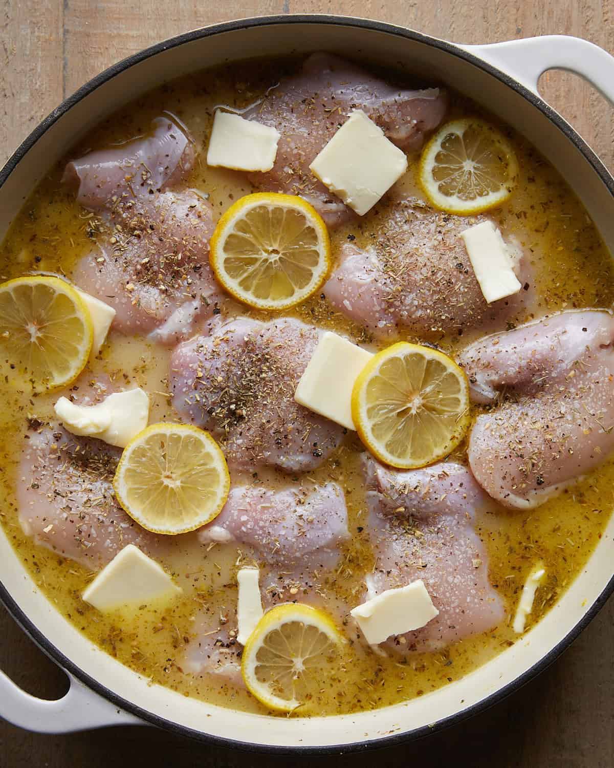 Lemon chicken and rice assembled with folded chicken thighs, butter, lemon slices, and seasoning before baking.